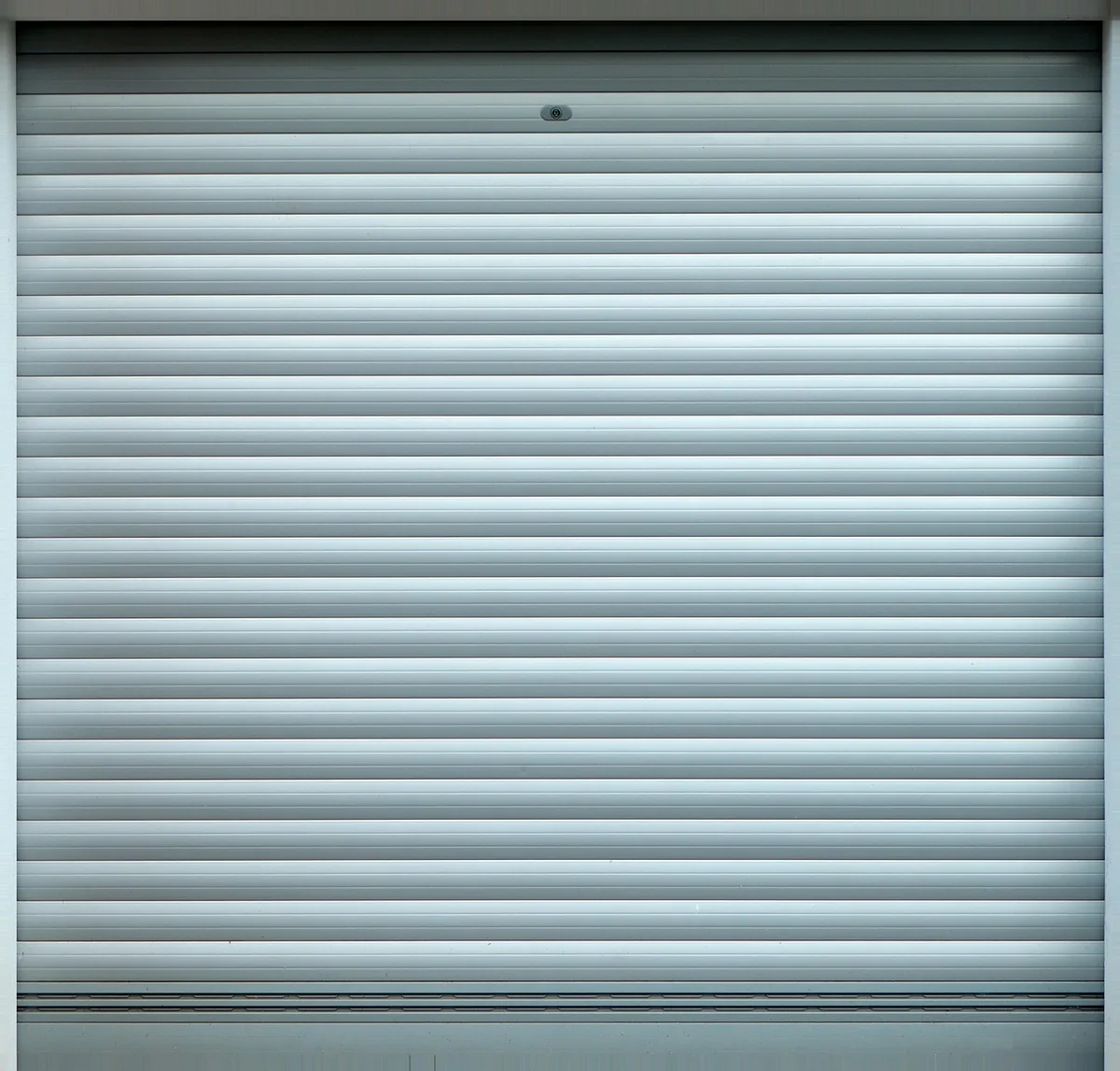 Hands holding the bottom slat of an unbranded roller shutter to reveal an identification sticker on the inner edge, well-lit interior