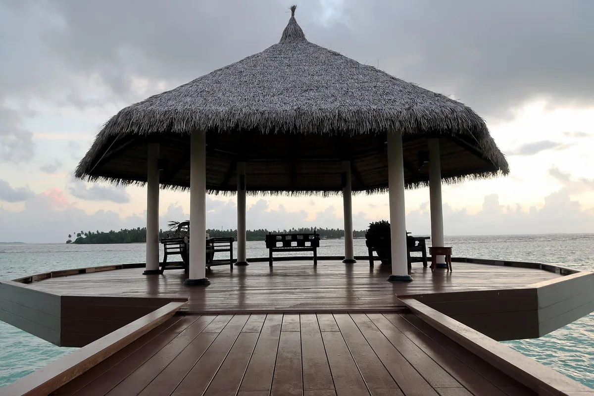 Bright daytime scene of an octagonal wooden kiosk with shingles roof and decorative trim, no people visible