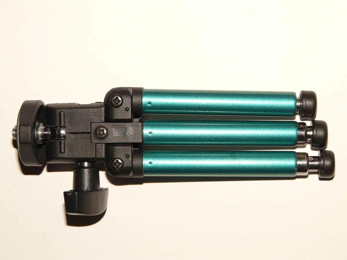 tripod-mounted rotary laser on a worksite, anonymous hands adjusting height, wheelbarrow and building materials in background