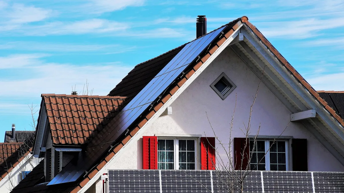 Roof with several unbranded solar panels mounted at an angle under a clear blue sky, no people, suburban houses in background
