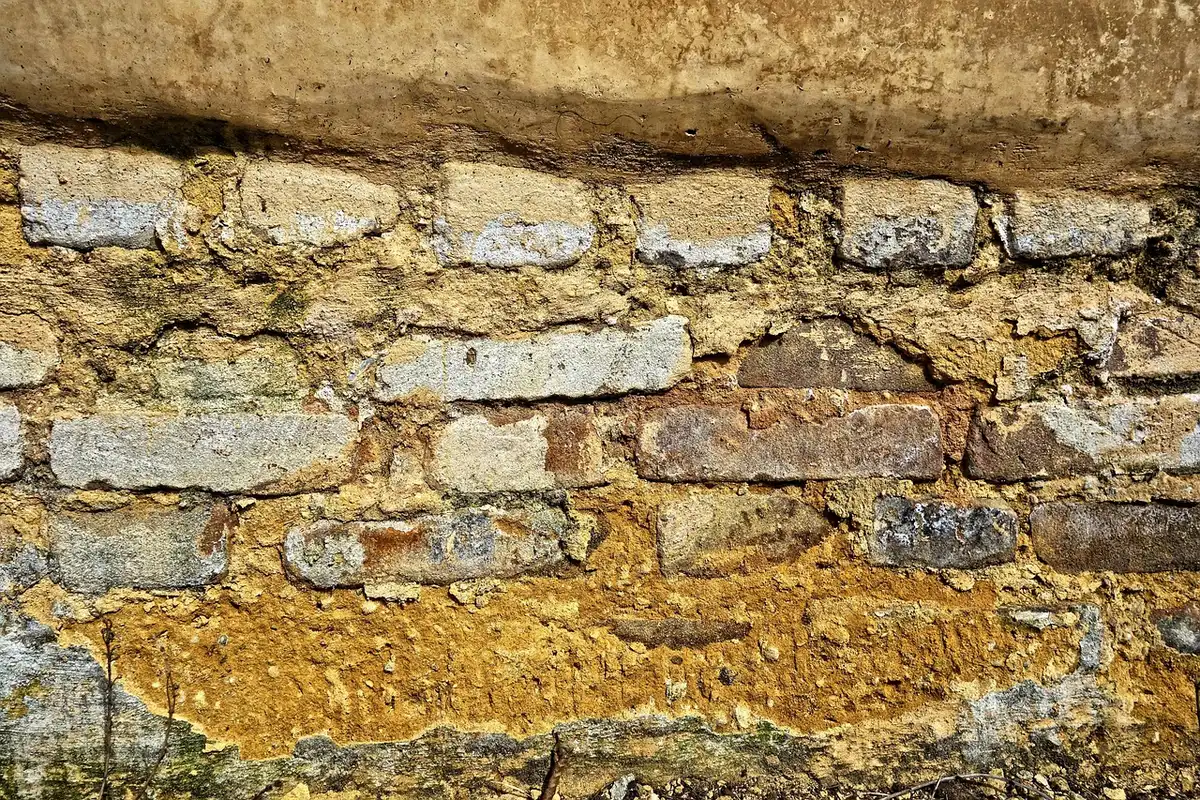 Hands rubbing a sanding block along a textured interior wall, small dust visible on floor