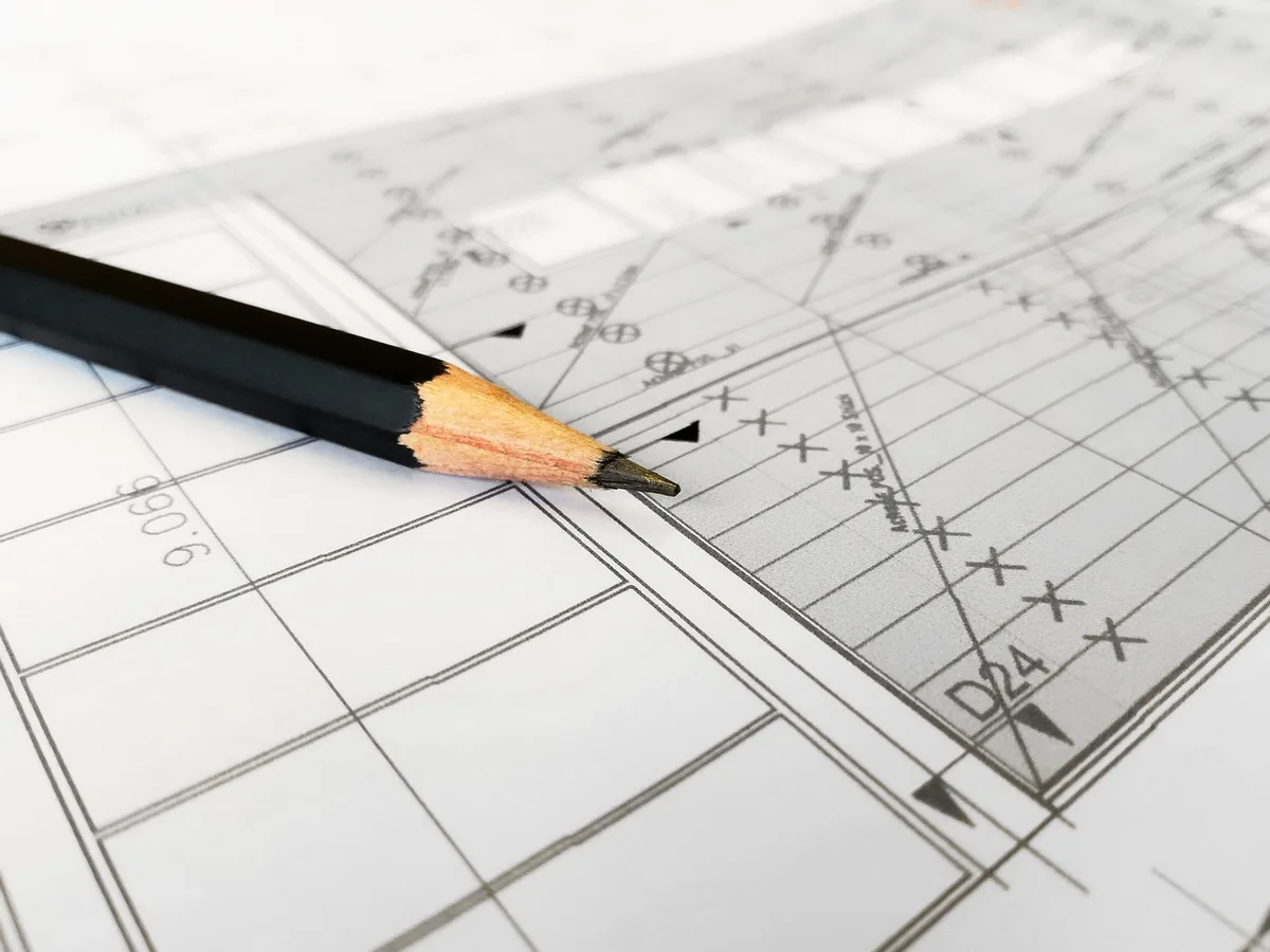 Clear daytime scene of a workbench with wooden beam plans, measuring tape, and a folded permit application form on the table
