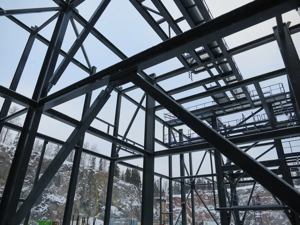 bright workshop with unbranded steel beams and plans on a table, hands pointing at drawing