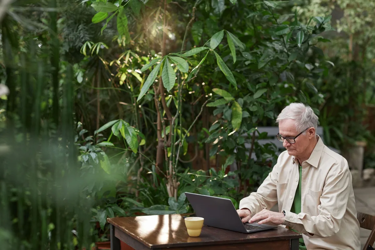 A well-lit small wood garden office interior with desk, chair, bookshelf and a window showing a green garden outside
